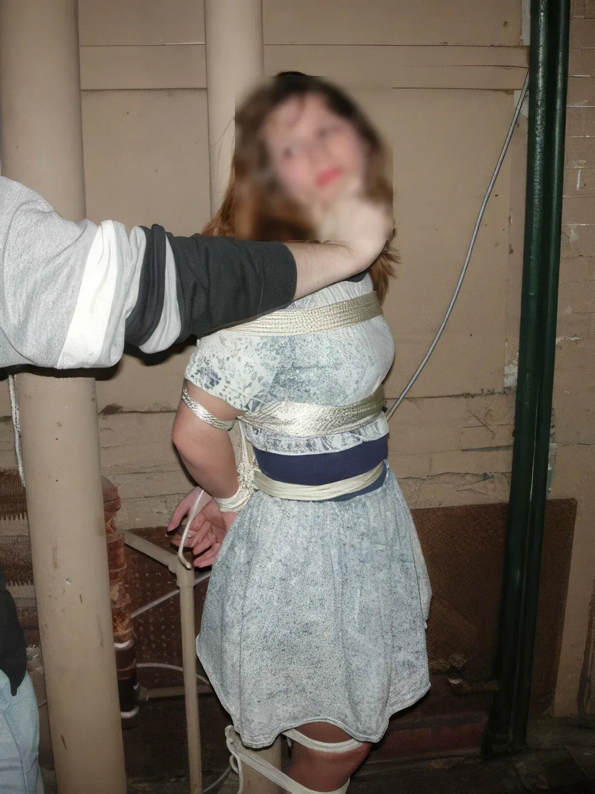 Person with blurred face restrained with tape in an indoor kink setting, reflecting privacy-aware BDSM dating.